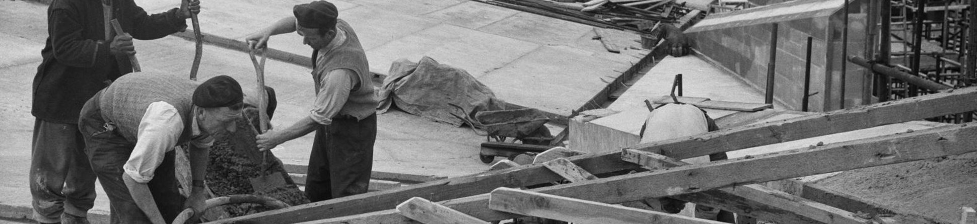 Black and white photo of three men pouring concrete. They aren't wearing any hard hats or high-vis clothing.