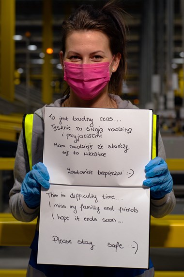 Photo of a woman holding up a handwritten sign in Polish and English "This is difficult time... I miss my family and friends. I hope it ends soon... Please stay safe"