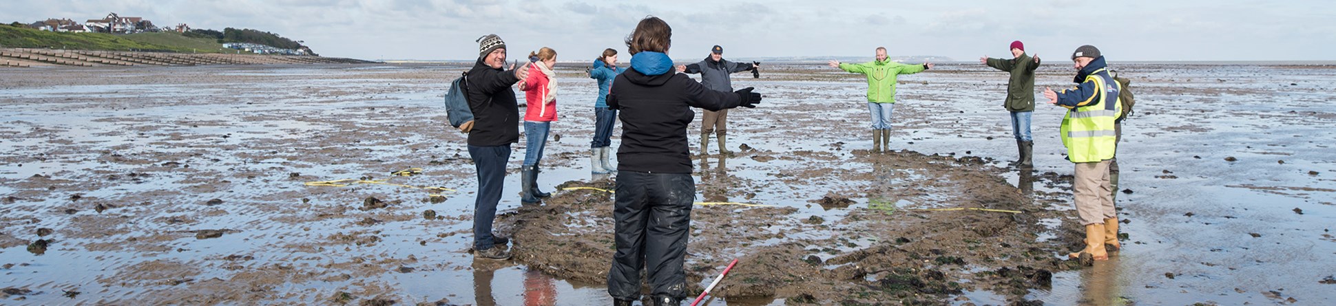 A group of people stood on a wet sandy beach forming a circle.