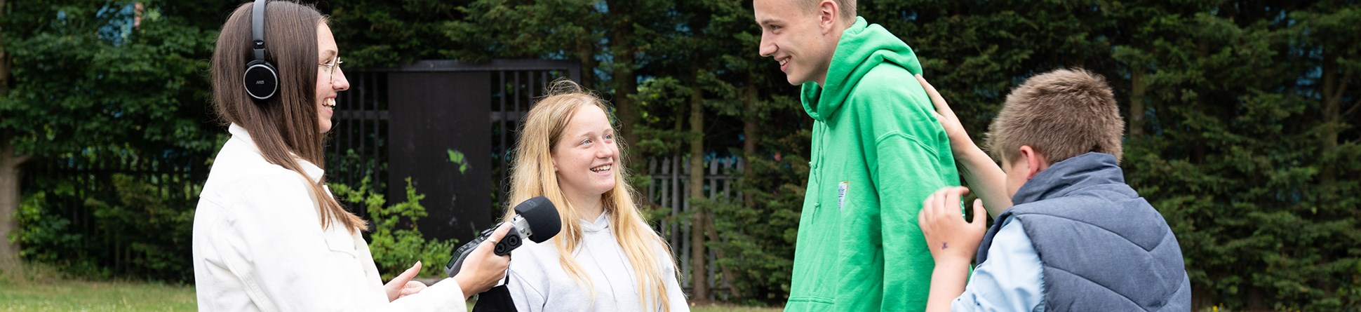 A woman holding a microphone and wearing headphones interviewing three other people