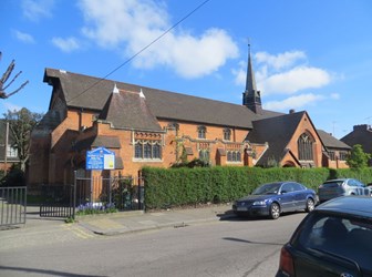 Red brick church with a small spire and a hedge in front.