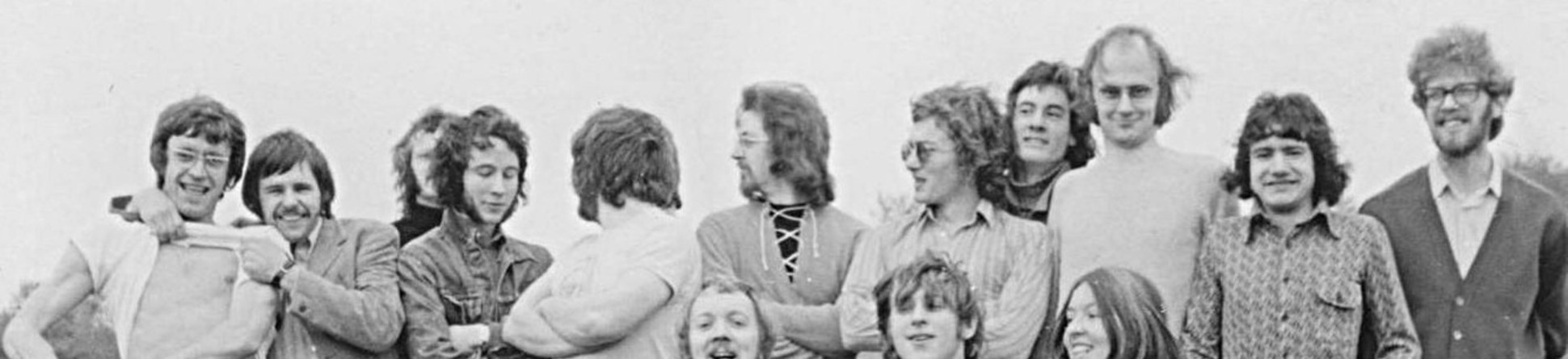 Black and white photo of a group of young men and one woman in high spirits posing for a post-match photo.