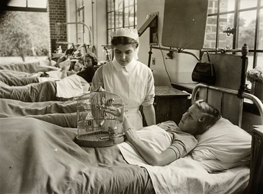 A patient with her pet budgerigar in a cage, which sits on her hand