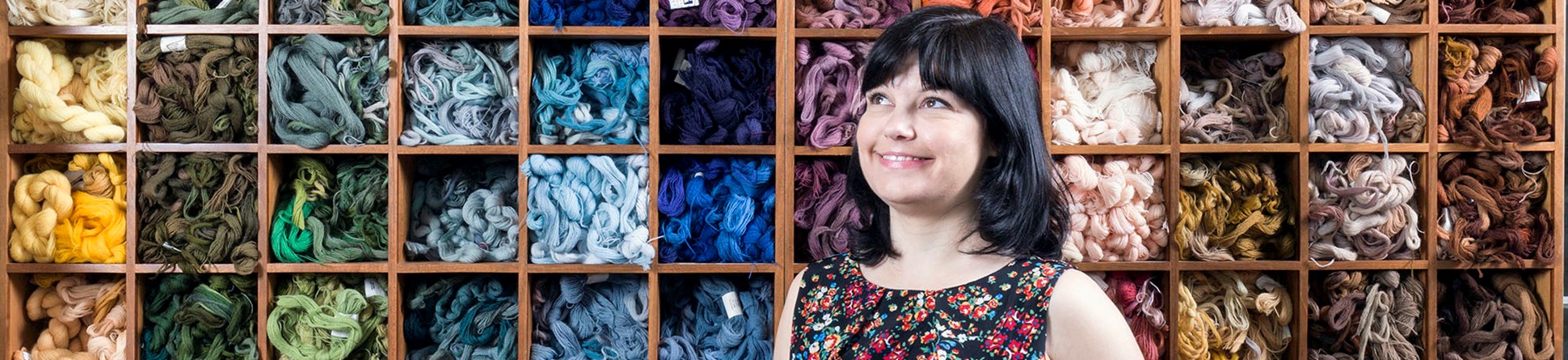 Young woman photographed in front of box shelving full of carefully organised embroidery thread.