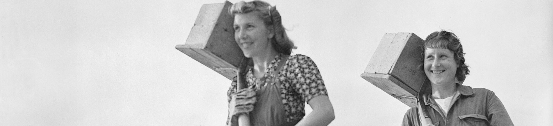 Black and white image of 2 women carrying bricks