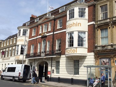 View of the Dolphin Hotel a brick and white stone building with a central archway you can walk through. There are two large bay windows on each side on the second and third floors