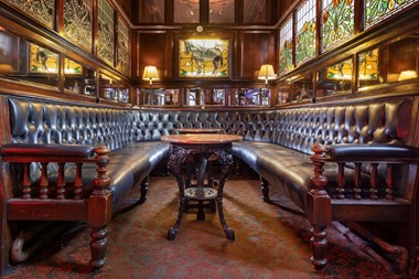 Leather bench seating and wall panels with mirrored surround and stained glass windows behind.