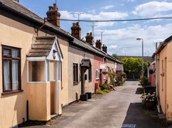 A double row of single storey cottages, in a range of colours, with arched porches.