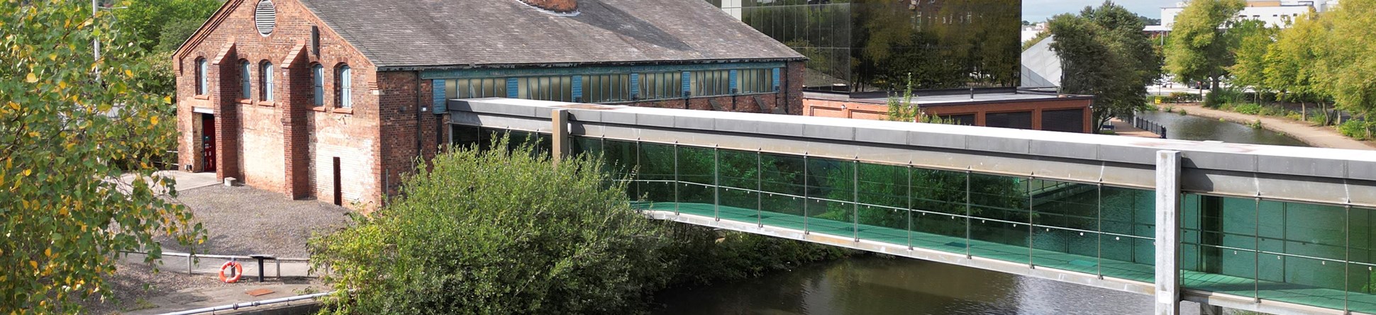 A glass-enclosed walkway crossed a canal to reach a red brick building, with a modern glass building behind.