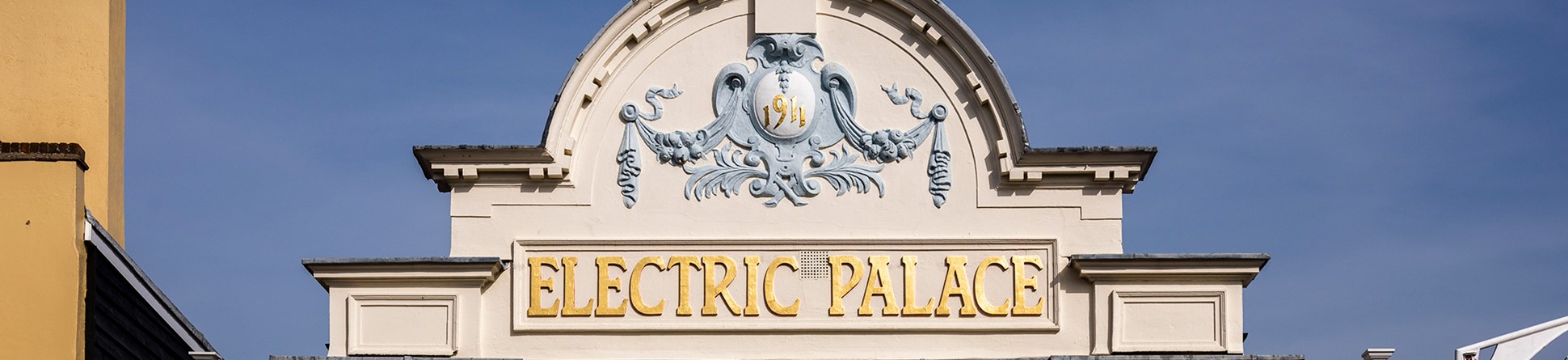 The facade at the top of the exterior entrance to the Electric Palace Cinema shows scrolling decoration and the words 1911 and Electric Palace within an arched top section of the facade.