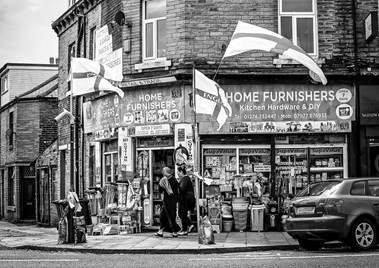 Exterior view of the Home Furnishers shop at 71 White Abbey Road, showing goods on display outside, and two people standing at the entrance.