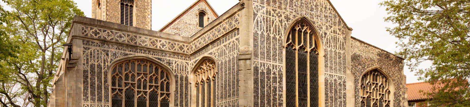 the image shows the front of the church, with its ornate brickwork and large arched windows. The church tower can be seen behind.