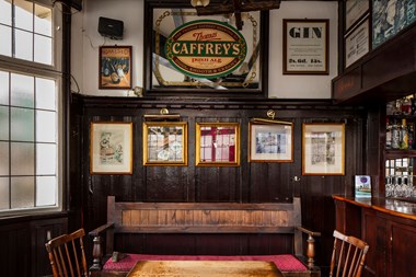 Interior view of a tavern with a freestanding bench, table and chairs and imitation wood panelling.