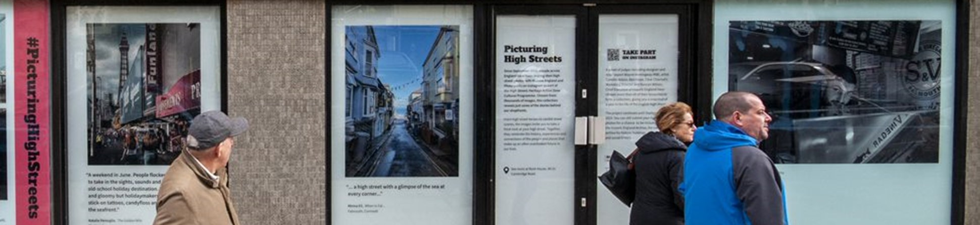 Three people and a dog walking past a building with Picturing High Streets images being exhibited in the windows.