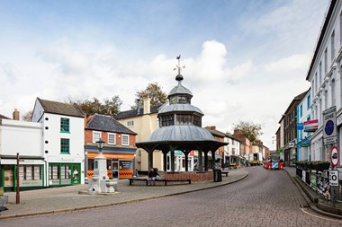 A view up a cobbled street, with granite water fountain and market cross in the foreground.