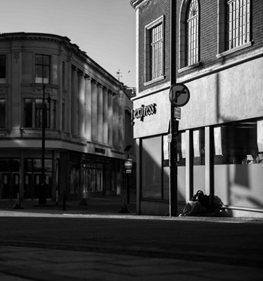 Black and white image of someone sitting on the ground outside a supermarket